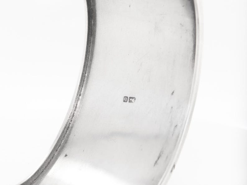 Puede incluir: Un brazalete de plata con un sello en el interior.