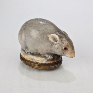 May include: A ceramic trinket box shaped like a grey mouse with red eyes. The box is closed and has a brass hinge.