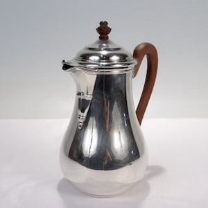 May include: A silver coffee pot with a wooden handle and a wooden knob on the lid.