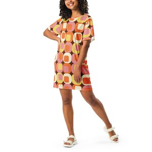 Könnte beinhalten: Eine Frau trägt ein kurzärmliges Kleid mit einem geometrischen Muster aus orangefarbenen, rosa, gelben und braunen Quadraten. Das Kleid hat einen Rundhalsausschnitt und eine lockere Passform.