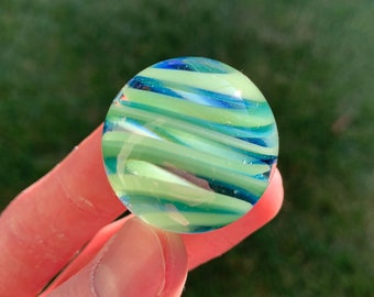 May include: A green and blue glass marble with swirling patterns.