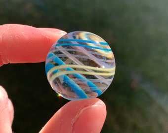 Peut inclure: Un marbre en verre transparent avec des rayures bleues et blanches. Le marbre est tenu entre deux doigts.