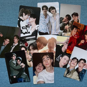 May include: A collection of glossy photo cards featuring various images of young men. The cards display portraits and candid shots, with a variety of poses and settings. The cards are arranged on a blue textured surface.
