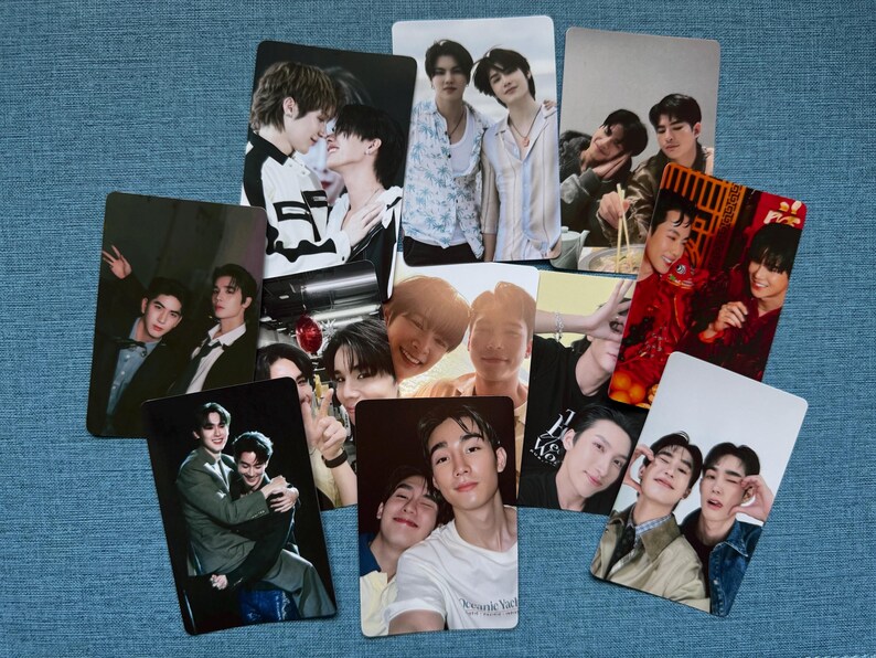 May include: A collection of glossy photo cards featuring various images of young men. The cards display portraits and candid shots, with a variety of poses and settings. The cards are arranged on a blue textured surface.