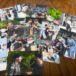 May include: A collection of rectangular photo cards featuring images of people in military uniforms, some holding bouquets of flowers. The cards are arranged on a wooden surface, with various scenes and individuals depicted.