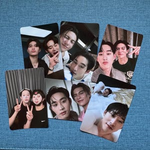May include: A collection of photo cards featuring various individuals in casual poses. The cards display a variety of facial expressions and gestures, with some individuals making peace signs or playful faces. The cards are arranged on a blue surface.