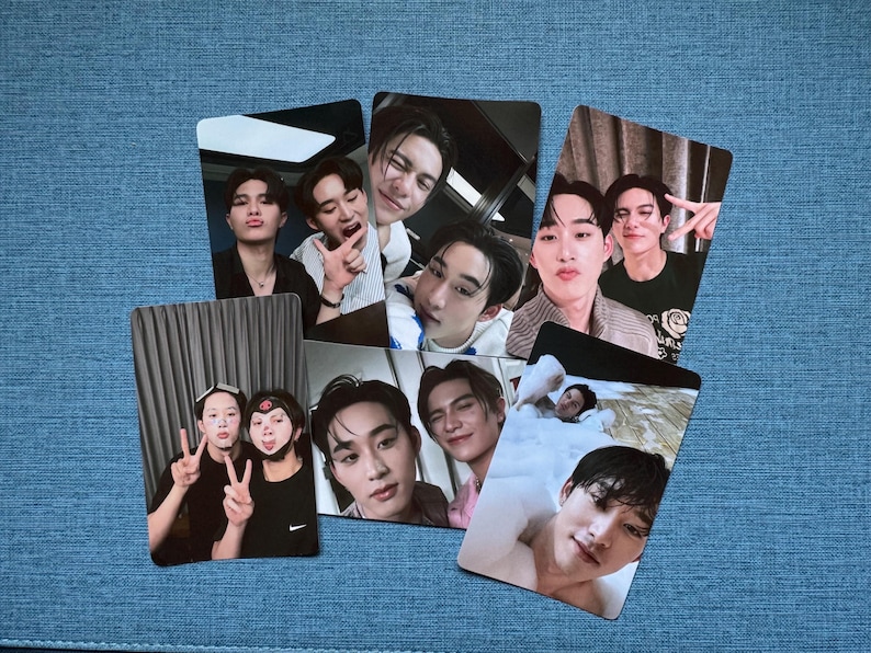 May include: A collection of photo cards featuring various individuals in casual poses. The cards display a variety of facial expressions and gestures, with some individuals making peace signs or playful faces. The cards are arranged on a blue surface.