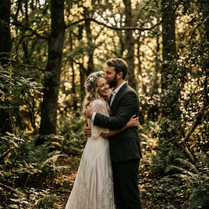 Puede incluir: Un vestido de novia de encaje blanco con mangas cortas y falda fluida, combinado con una chaqueta de traje y pantalones de color gris oscuro. El vestido presenta detalles de encaje en el corpi&ntilde;o y las mangas, mientras que el traje es liso.