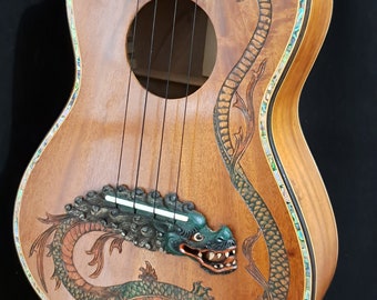 May include: A wooden ukulele with a green and brown dragon inlay on the body and a floral design on the neck. The ukulele has a mother-of-pearl inlay around the edge of the body.