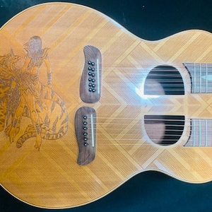 May include: A wooden acoustic guitar with a decorative inlay of a woman riding a tiger. The guitar has two sound holes and a natural wood finish.