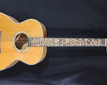 May include: A brown acoustic guitar with intricate gold inlay designs on the body and neck. The guitar features a lion design on the soundboard and a gold-colored headstock.