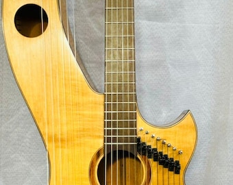 May include: A light brown acoustic guitar with a unique design. The guitar has a round body with a smaller, round sound hole. The neck of the guitar is attached to the body at an angle, creating a distinctive shape. The guitar has a total of 12 strings, with 6 strings on the traditional guitar neck and 6 strings on the harp-like neck.