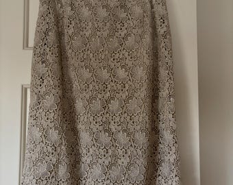 Puede incluir: Una falda de encaje beige con estampado floral. La falda es de largo hasta la rodilla y tiene un dobladillo festoneado.