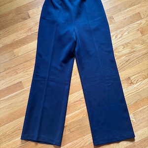 May include: Navy blue wide-leg pants. The pants have a high waist and a straight, relaxed fit. The fabric appears to be a smooth, solid color. The pants are laid flat on a wooden surface.