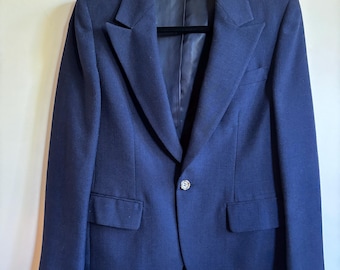 May include: A navy blue blazer with a classic design, featuring a notched lapel, two front pockets, and a single button closure. The blazer is hanging on a black hanger against a neutral background. The jacket appears to be made of a wool blend.