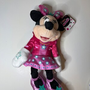 Pu&ograve; includere: Minnie Mouse di peluche rosa e turchese con un vestito rosa con stelle bianche e un fiocco turchese. Il peluche ha un'etichetta che dice "Disney Junior Minnie"