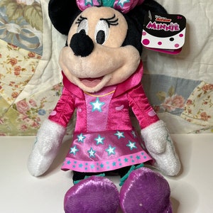 Pu&ograve; includere: Peluche rosa Minnie Mouse con un vestito rosa con stelle bianche e un fiocco rosa con stelle bianche. Il giocattolo ha un'etichetta che dice "Disney Junior Minnie" e "2+".
