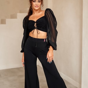 May include: A black crop top with a lace-up front and sheer long sleeves. The top is paired with black wide-leg trousers.
