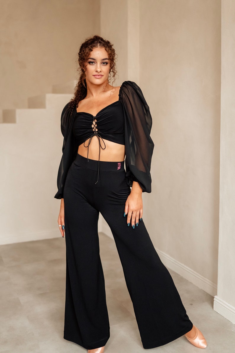 May include: A black crop top with a lace-up front and sheer long sleeves. The top is paired with black wide-leg trousers.