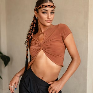 Puede incluir: Una mujer con un top corto marr&oacute;n con un detalle de torsi&oacute;n y pantalones negros. Lleva una diadema trenzada en marr&oacute;n y negro.