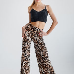 May include: A woman wearing a black crop top and leopard print trousers. She is standing with her hands on her hips and looking at the camera.