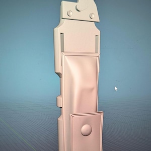 Op de afbeelding: Een lichtgekleurd, verticaal object met een complex ontwerp. Het heeft een rechthoekig lichaam met een zakje en een afgeronde knop. De bovenkant heeft een unieke vorm met twee cirkelvormige elementen. Het object staat tegen een blauwe achtergrond.