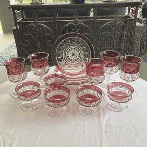 Puede incluir: Un juego de diez platos de postre de vidrio vintage con un diseño rojo y transparente. Los platos están dispuestos sobre un mantel blanco.
