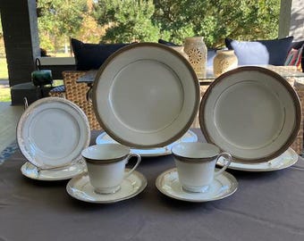 May include: A set of white porcelain dinnerware with gold trim. The set includes a dinner plate, a salad plate, a teacup, and a saucer.