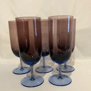 Puede incluir: Juego de seis copas de vino de vidrio teñido de púrpura con bases azules. Las copas están dispuestas en semicírculo.