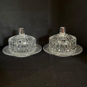 Puede incluir: Dos mantequilleras de vidrio transparente con tapas y platos a juego. Las mantequilleras tienen un patrón de diamante.
