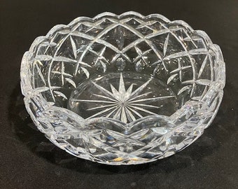 May include: A clear glass bowl with a cut crystal design. The bowl has a scalloped edge and a starburst pattern in the center.