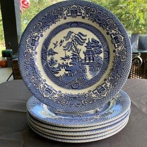Puede incluir: Un juego de seis platos de cena de cerámica azul y blanco con un patrón de sauce tradicional. Los platos tienen un fondo blanco con un sauce azul, un puente y una pagoda.