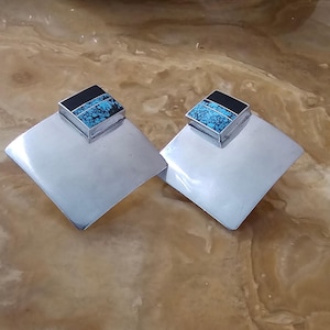 May include: A pair of silver square earrings with turquoise and black inlay.