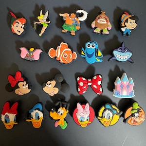 Peut inclure: Une collection de 20 breloques de chaussures de personnages de dessins animés colorés mettant en scène des personnages de films Disney comme Le Monde de Nemo, Peter Pan et Mickey Mouse.