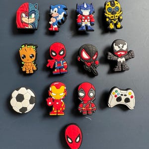 Puede incluir: Una colección de 13 amuletos de zapatos de personajes de dibujos animados coloridos, que incluyen Sonic the Hedgehog, Spiderman, Iron Man, Deadpool y un balón de fútbol.