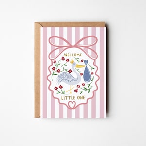 May include: A greeting card with a stork carrying a baby in a blue bundle, surrounded by flowers. The card has pink and white stripes and the words "WELCOME LITTLE ONE". The card is in a brown envelope.