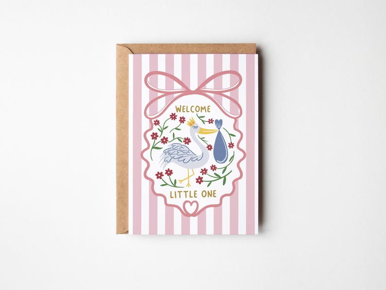 May include: A greeting card with a stork carrying a baby in a blue bundle, surrounded by flowers. The card has pink and white stripes and the words "WELCOME LITTLE ONE". The card is in a brown envelope.