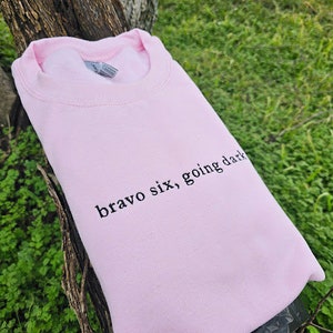 Puede incluir: Una sudadera rosa de cuello redondo con el texto "bravo six, going dark" impreso en negro.