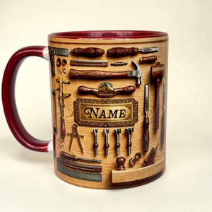 Könnte beinhalten: Keramikbecher mit weinrotem Griff und Rand, mit einem Design verschiedener Holzbearbeitungswerkzeuge, die auf einem Holzgrund angeordnet sind. Der Becher enthält das Wort "NAME" in einem goldfarbenen Rahmen.