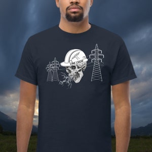 Può includere: Una t-shirt blu navy con una grafica bianca di uno scheletro che indossa un casco da lavoro con la scritta "Line Crew". Lo scheletro è circondato da linee elettriche.