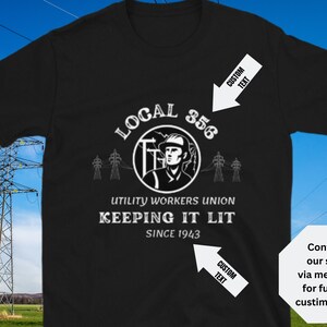 Può includere: Maglietta nera con una grafica bianca di un lavoratore di pubblica utilità di fronte a linee elettriche. Il testo recita "Local 356 Utility Workers Union Keeping It Lit Since 1943".