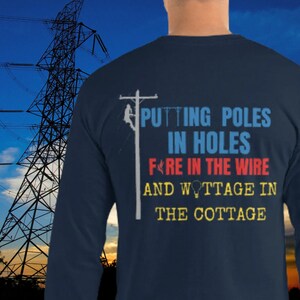Può includere: Una maglietta a maniche lunghe blu navy con una grafica di un palo della linea elettrica e il testo "Putting poles in holes, fire in the wire, and wattage in the cottage".