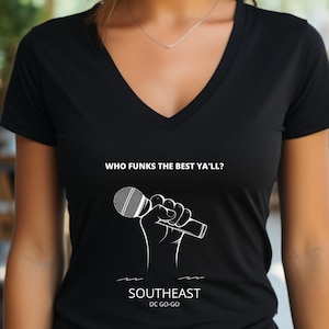 Op de afbeelding: Zwart V-hals T-shirt met witte tekst die "Who Funks the Best Ya'll?" luidt en een afbeelding van een hand die een microfoon vasthoudt. Onder de afbeelding staat de tekst "Southeast DC Go-Go."