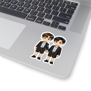 May include: A sticker featuring two cartoon figures in matching outfits. The figures are dressed in black blazers, shorts, and white shirts. They are holding hands and have dark hair and skin. The sticker is placed on a laptop.