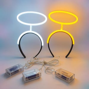 May include: Two light-up halo headbands, one white and one yellow, with black headbands and clear battery packs. The halos are oval-shaped and connected to the headband by a vertical bar. The headbands are lit with LED lights.