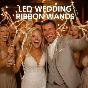 May include: A group of people, including a bride and groom, are smiling and holding LED wedding ribbon wands. The wands have white ribbons and small lights. The text "LED WEDDING RIBBON WANDS" is at the top of the image.