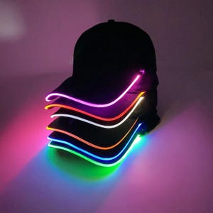 May include: A stack of black baseball caps with colourful LED lights around the brim. The lights are in different colours, including purple, orange, white, blue, and green.