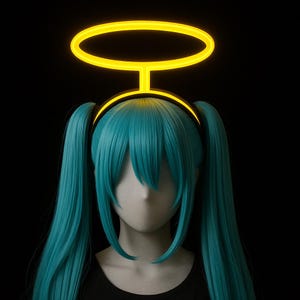May include: A mannequin head with long, turquoise pigtails and a black top. A glowing yellow halo is positioned above the head. The background is solid black, creating a striking contrast with the bright colors of the wig and halo.