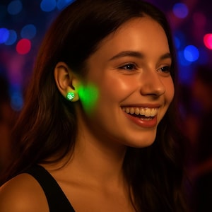 May include: A woman wearing a pair of glowing green stud earrings. The earrings emit a bright green light, illuminating the area around the ear. The woman is smiling, with a blurred background of colorful lights.