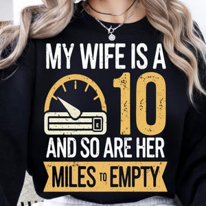 May include: Black sweatshirt with the text "MY WIFE IS A 10 AND SO ARE HER MILES TO EMPTY" in white and yellow. The design includes a speedometer graphic.